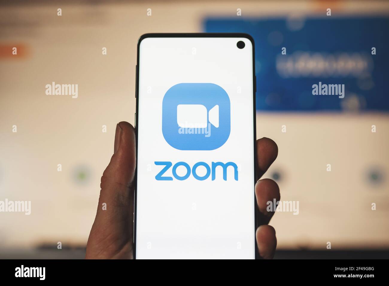 Mann hält ein Smartphone mit Zoom App-Logo mit verschwommenem Website-Hintergrund. Plattform für Video- und Audiokonferenzen Stockfoto