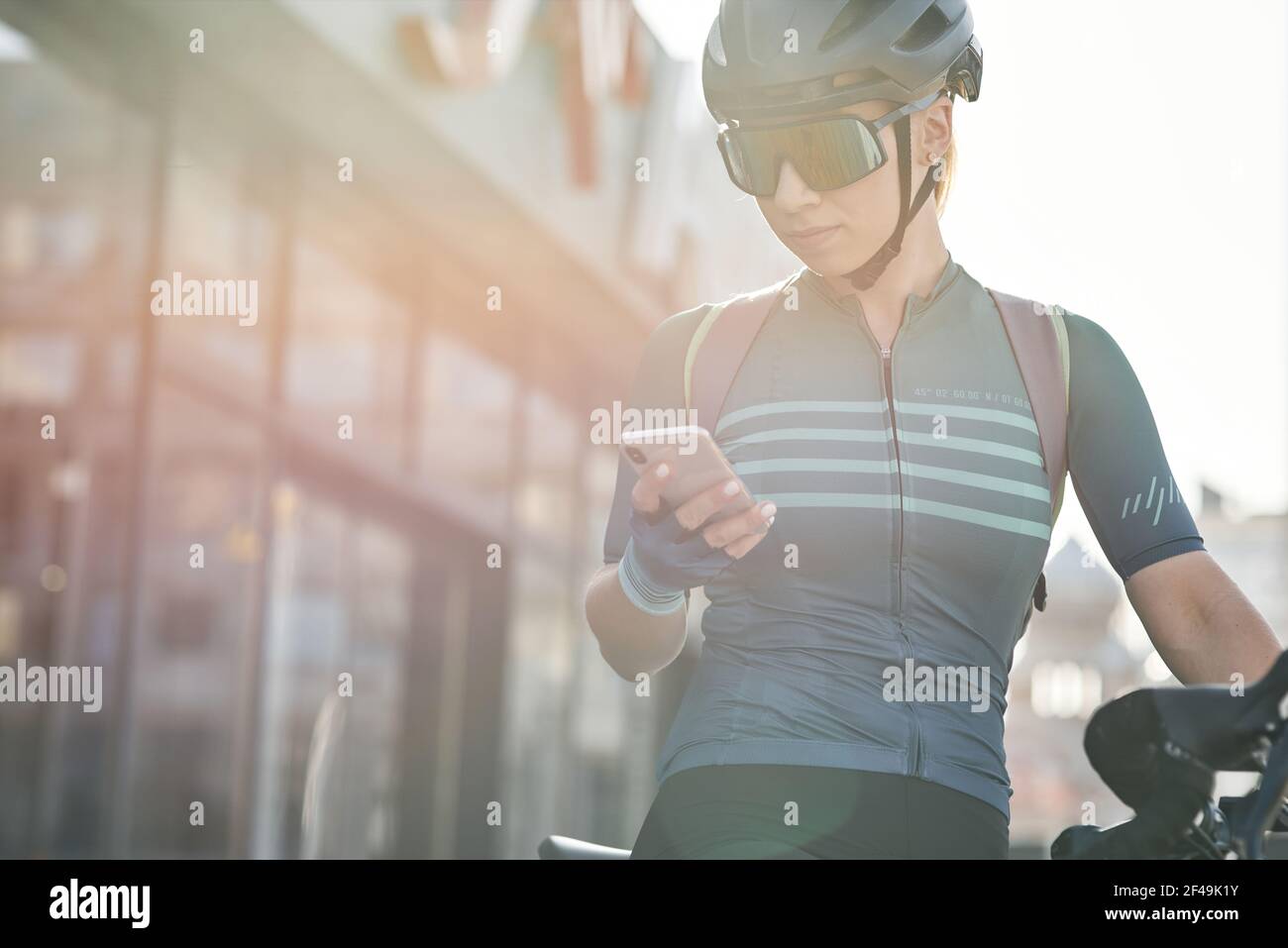 Radfahrerin in Schutzkleidung mit Smartphone, während Fahrrad in der Innenstadt fahren. Sportwoman Training, Training im Freien Stockfoto
