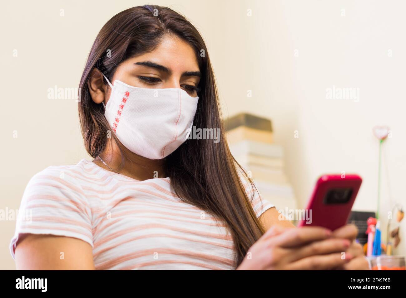 Ein junger ethnischer lateinamerikaner in einer medizinischen Maske mit Mobiltelefon Stockfoto