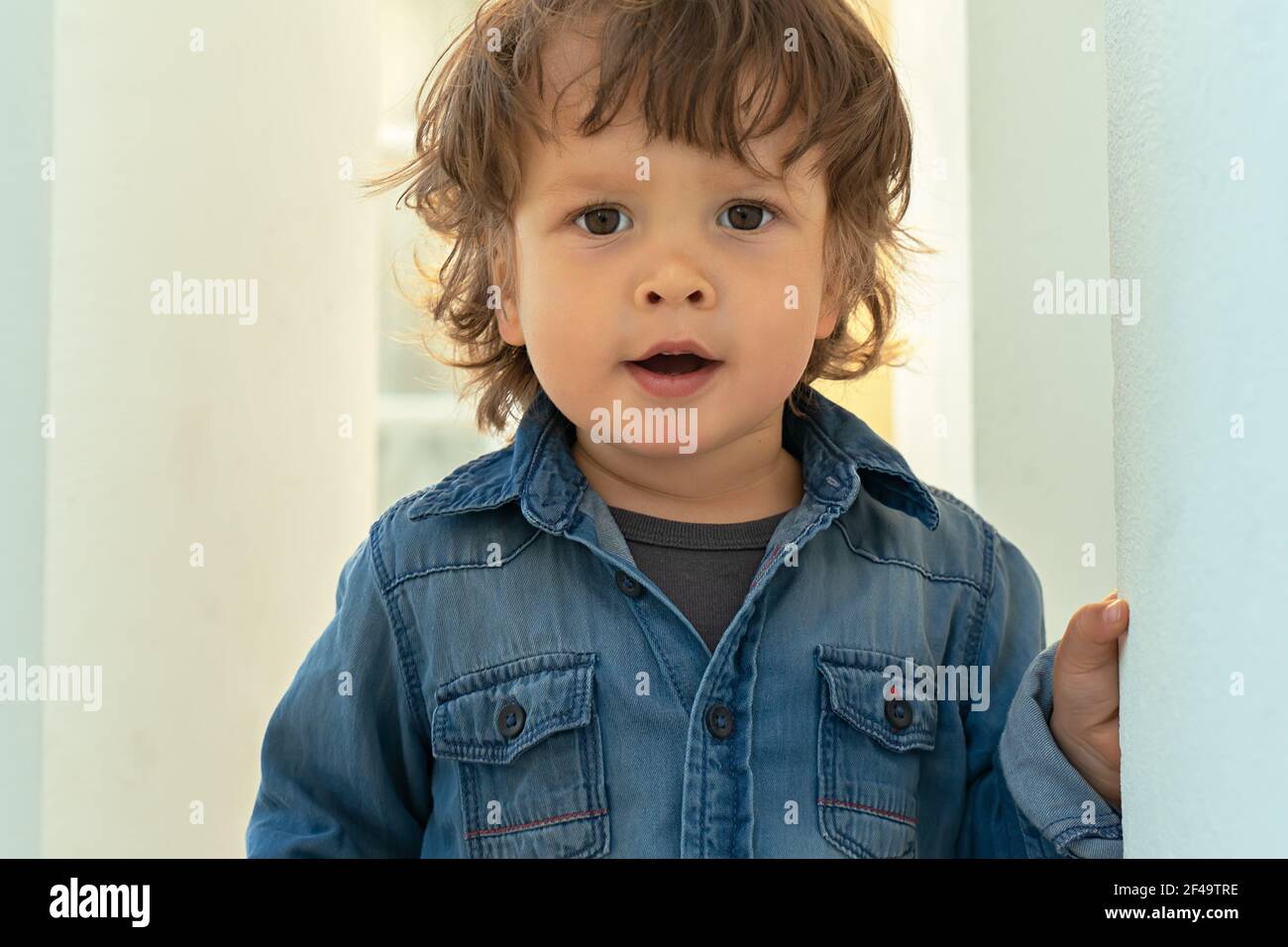 Nahaufnahme Porträt von modischen modernen kleinen Jungen mit langen Haaren und braunen Augen, Blick auf die Kamera auf weißem Hintergrund Stockfoto