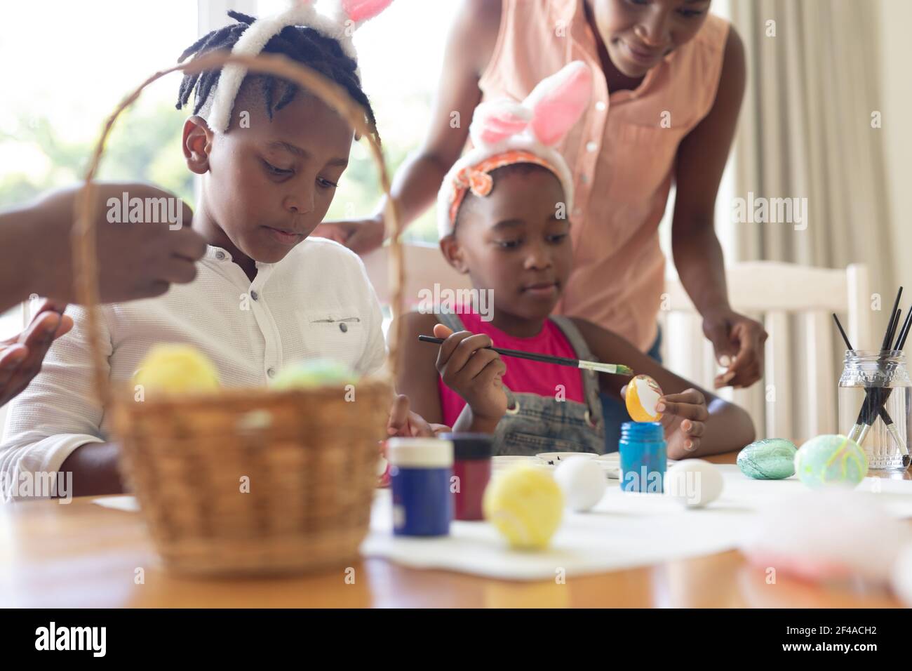 afroamerikanische Mutter mit Sohn und Tochter, die Hasenohren tragen Ostereier malen Stockfoto
