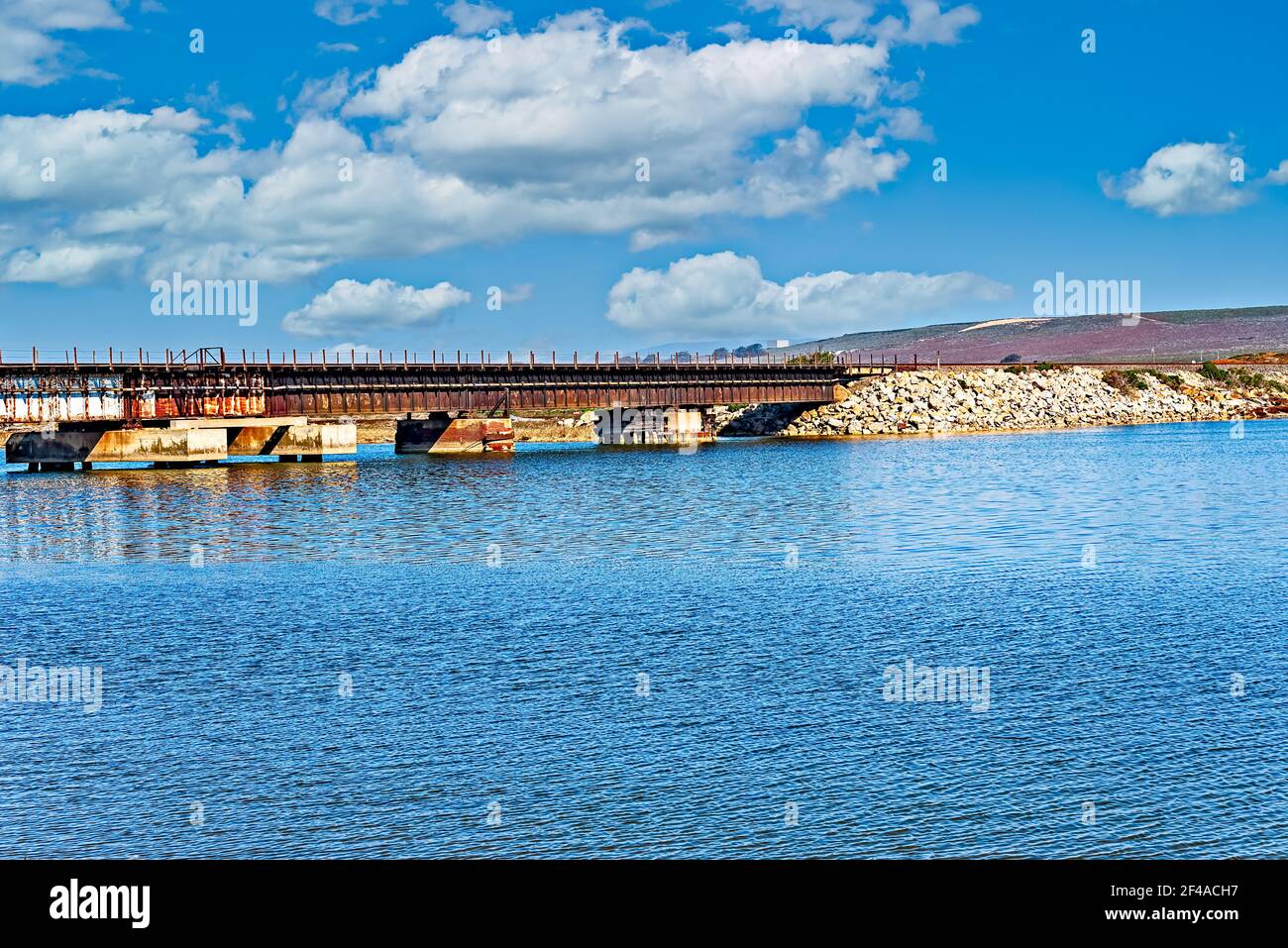 See mit Stahl- und Betonbrücke über die Bucht unter hellblauem Himmel mit weißen, flauschigen Wolken. Stockfoto