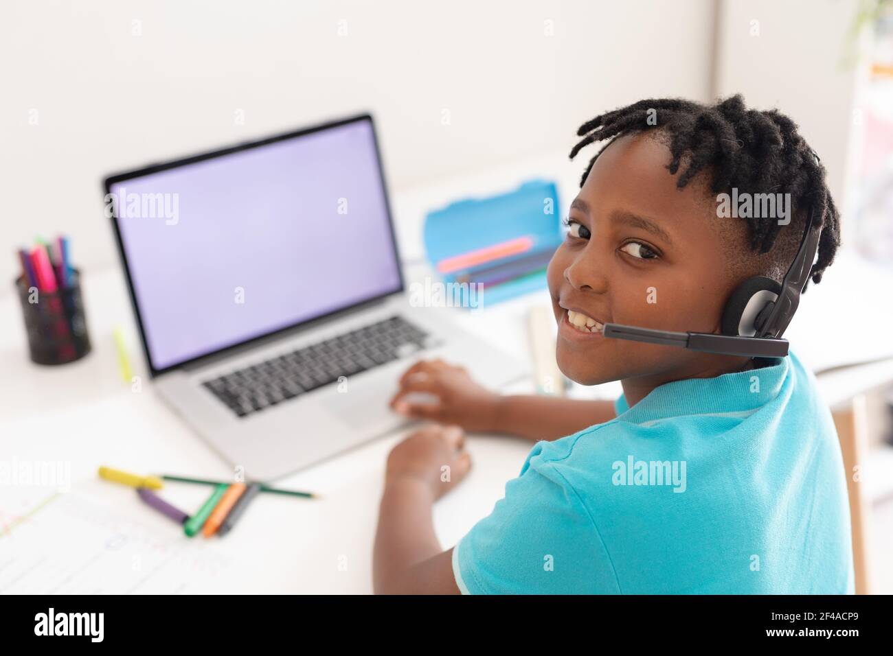 Porträt eines afroamerikanischen Jungen, der am Schreibtisch ein Headset trägt Laptop für Online-Schulunterricht Stockfoto