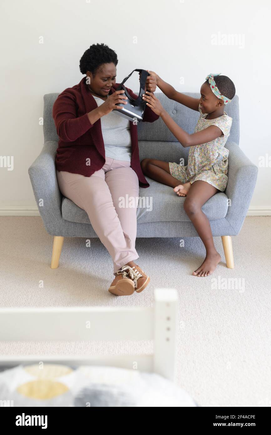 afroamerikanische Großmutter sitzt auf Couch setzen auf vr Headset Mit Hilfe der Enkelin Stockfoto