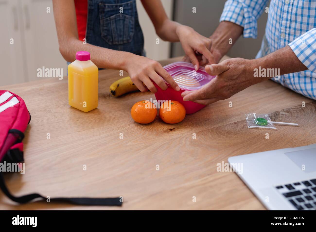 Mittelteil des kaukasischen Großvaters gibt Enkelin Lunchpaket und Lollipop In der Küche Stockfoto