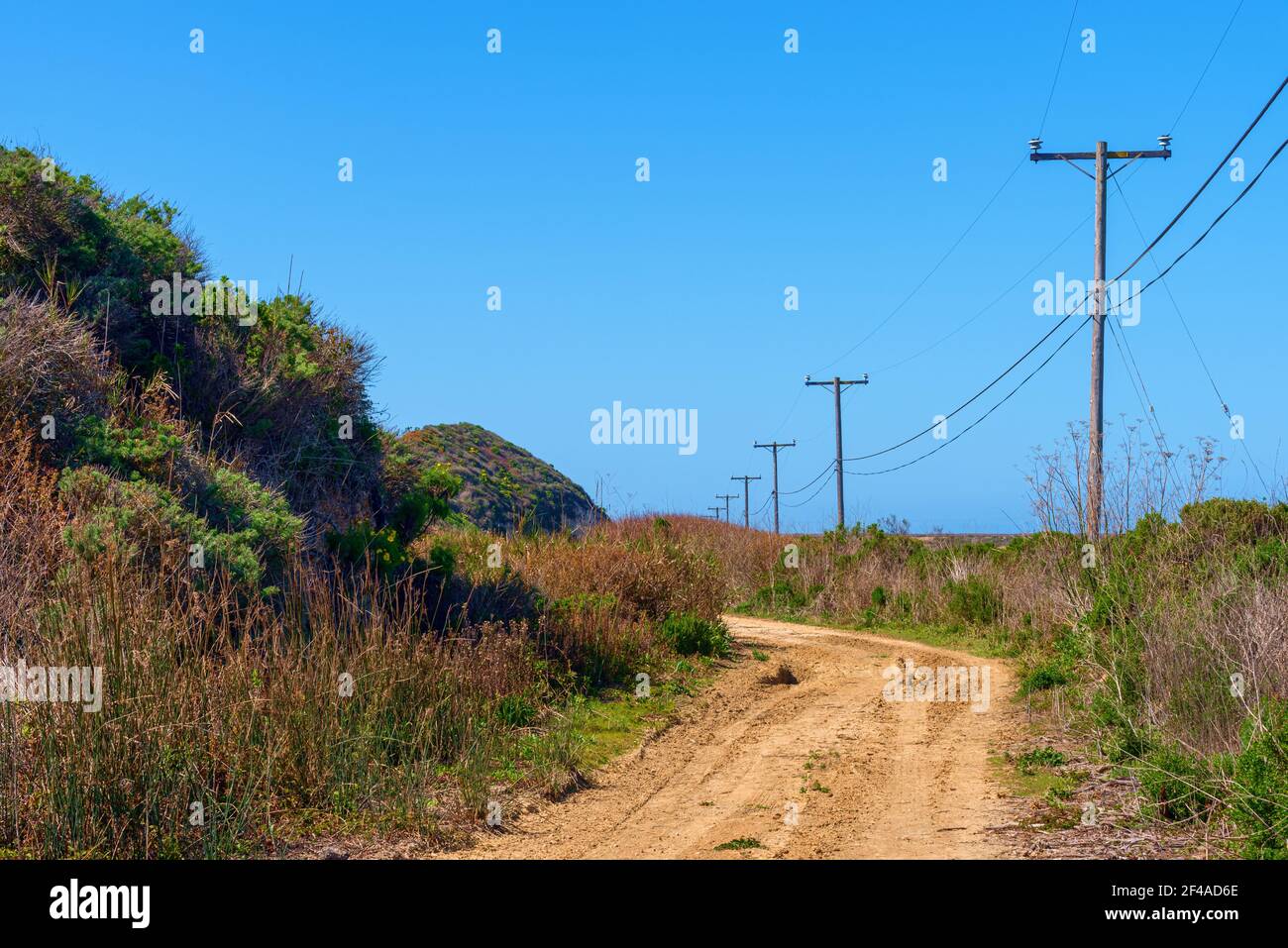 Rauer Feldweg kurvt Hügel mit Telefonmasten unter Blau Himmel Stockfoto
