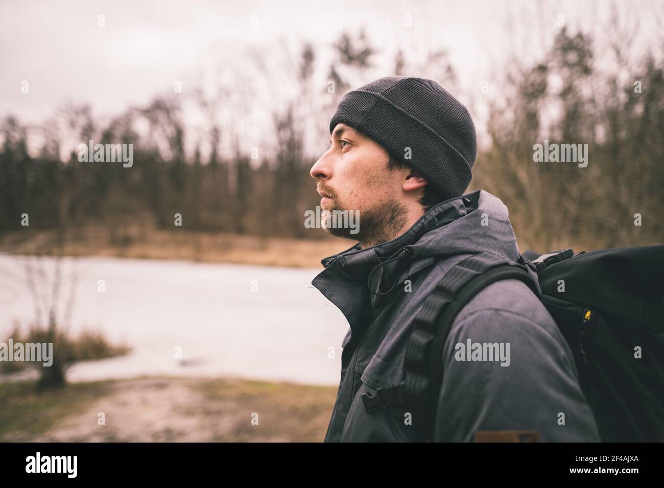 Einsamer trauriger Mann, der mit dem Rücken steht und auf den gefrorenen See im Wald schaut. Depression, schlechte Laune und Selbstmordgedanken. Ich brauche psychologische Hilfe Stockfoto