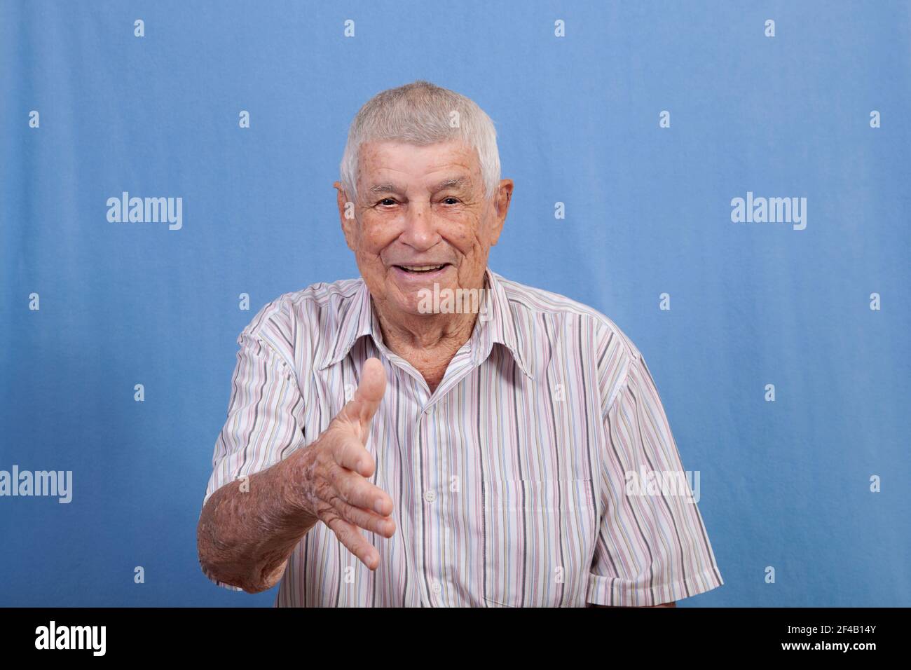 Aktiver glücklicher älterer Mann mit grauem Haar und einer sonnengeschädigten Haut, die sich ausstreckt, um die Hände beim Gruß zu schütteln, während sie lächelt. Stockfoto