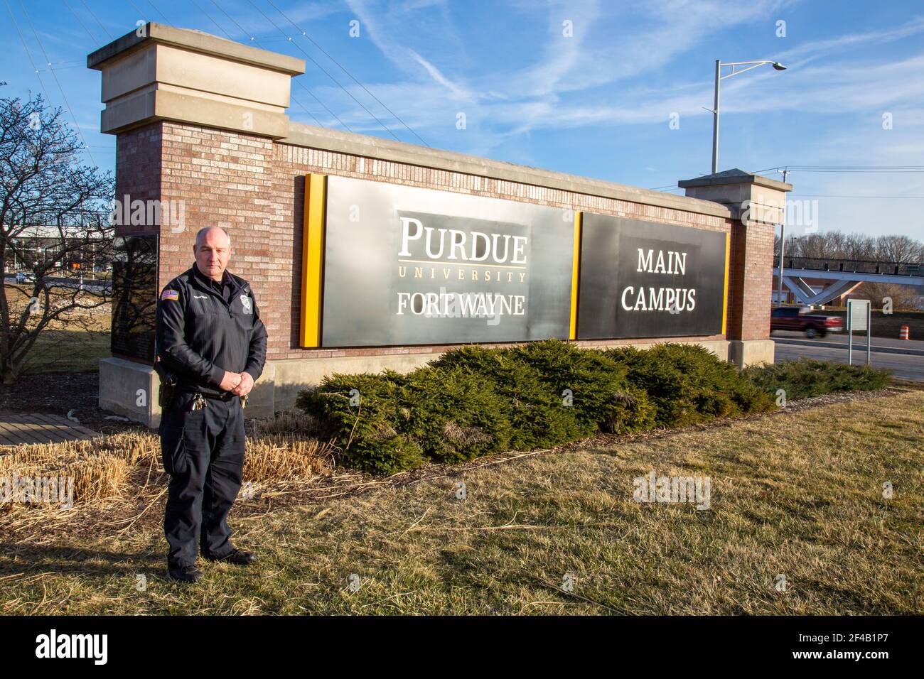Ein Polizeibeamter posiert auf dem Schild, das den Hauptcampus der Purdue University Fort Wayne bezeichnet. Stockfoto