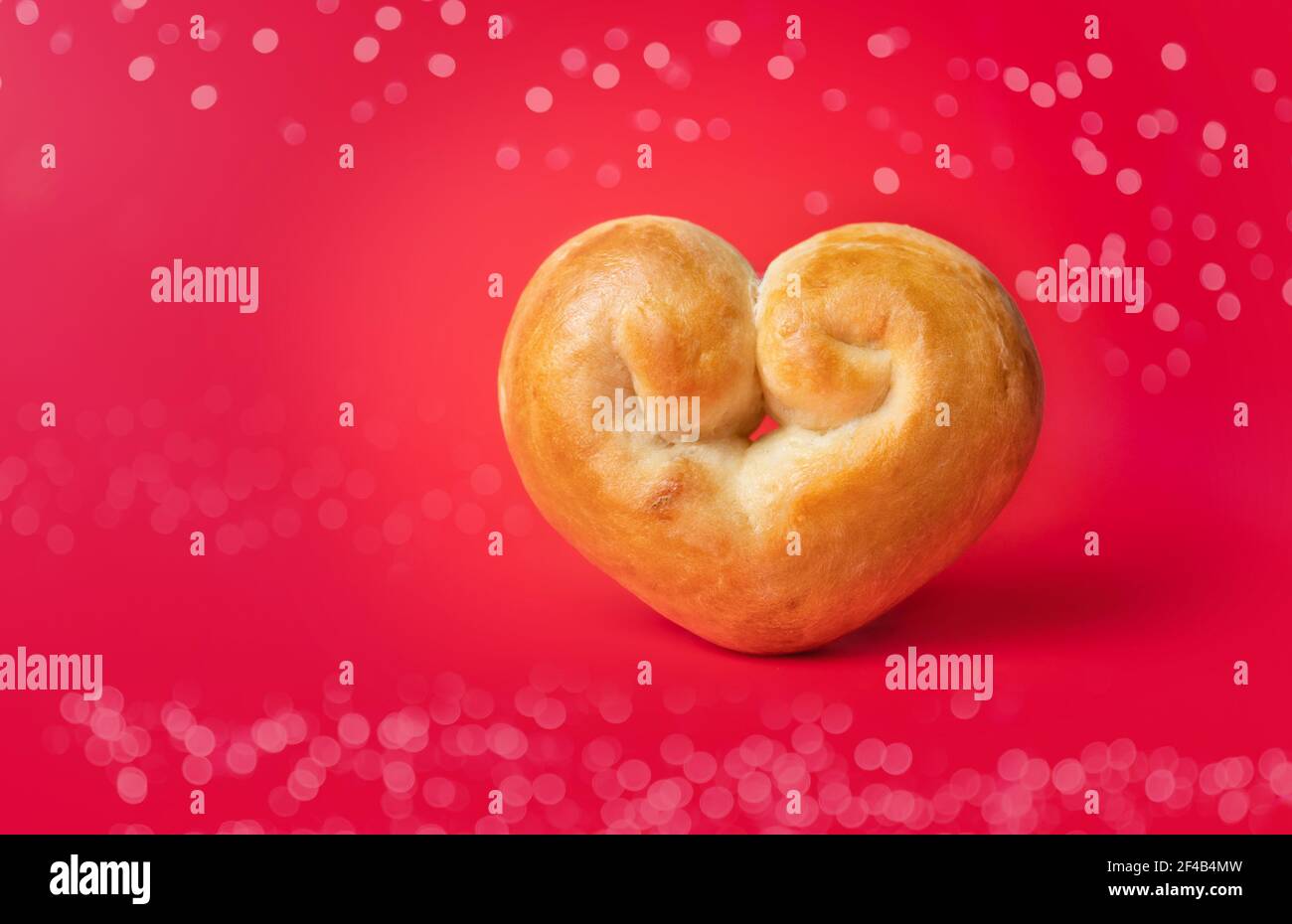 Romantisches Brotherz auf rotem Hintergrund mit Bokeh-Lichtern. Hefebrot Brötchen geformt wie ein Herz. Konzept für Valentinstag oder Backen mit Liebe.Traditio Stockfoto