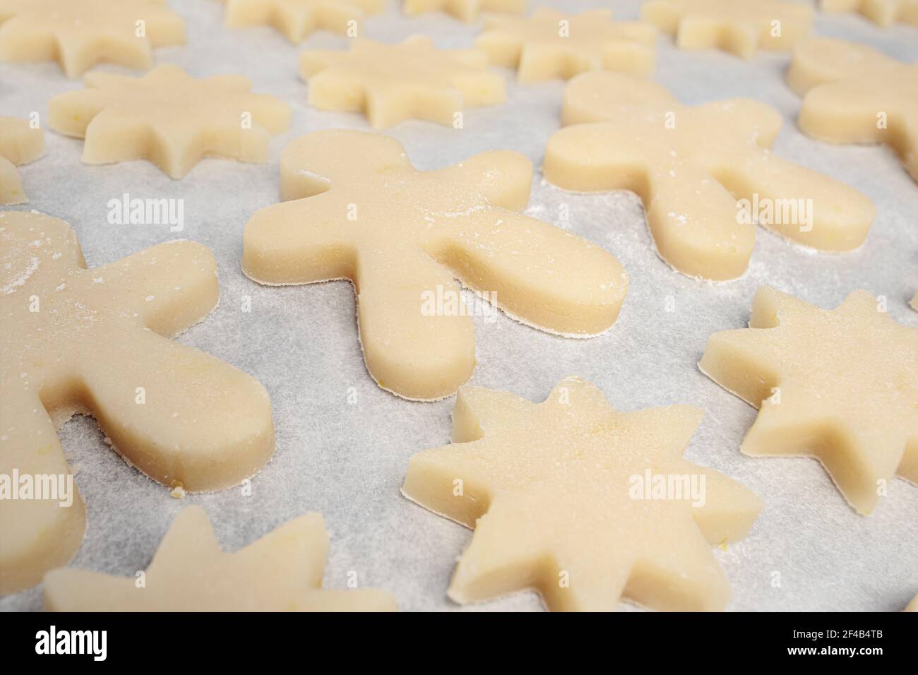 Viele kurze Brotzucker-Keks auf Pergamentpapier, fertig zum Backen. Nahaufnahme von ausgeschnittenen Keksen in Stern und Lebkuchen Mann Formen. Traditioneller Swis Stockfoto