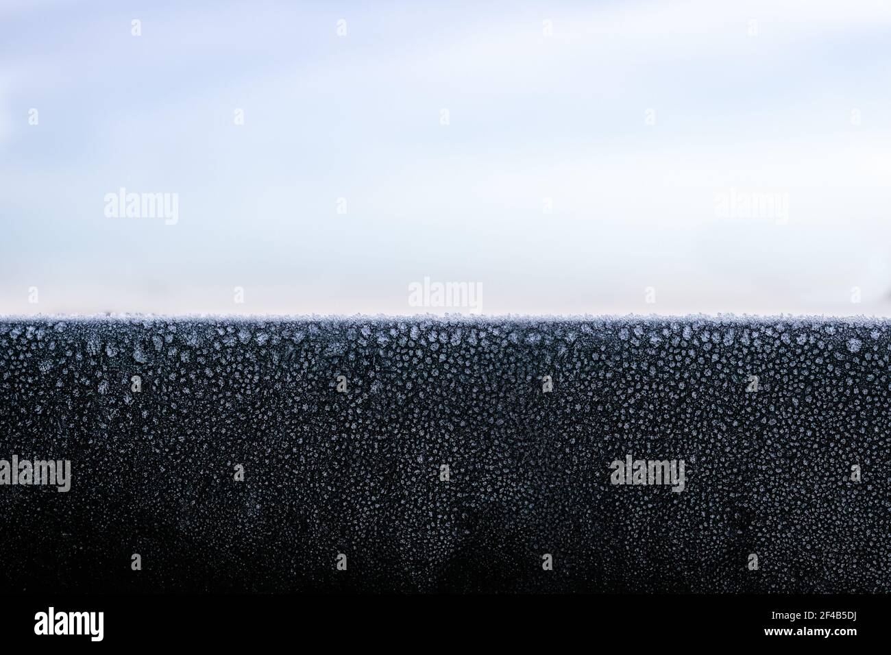 Schwarzes Dachmetall blinkt mit Frost oder Eiskristallen am frühen Morgen, in der Nähe des Sonnenaufgangs. Schöne dünne Schicht aus Eis auf festen Balg-Gefrierfläche wi Stockfoto