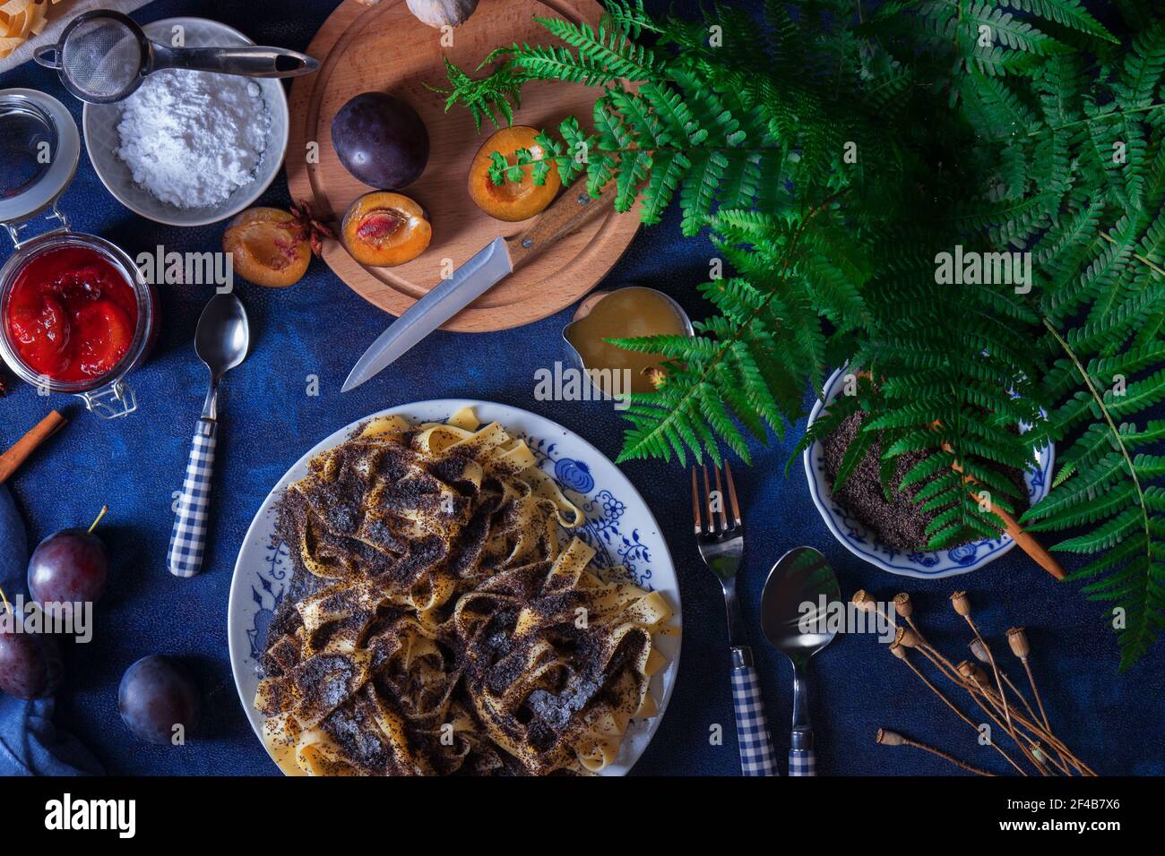 Süße Nudeln Dessert, Nudeln mit Mohn, Pflaumenkompott aus frischen Pflaumen, dunklen Hintergrund, blau Tisch mit frischen Blumen dekoriert. Trocken ganze Popp Stockfoto