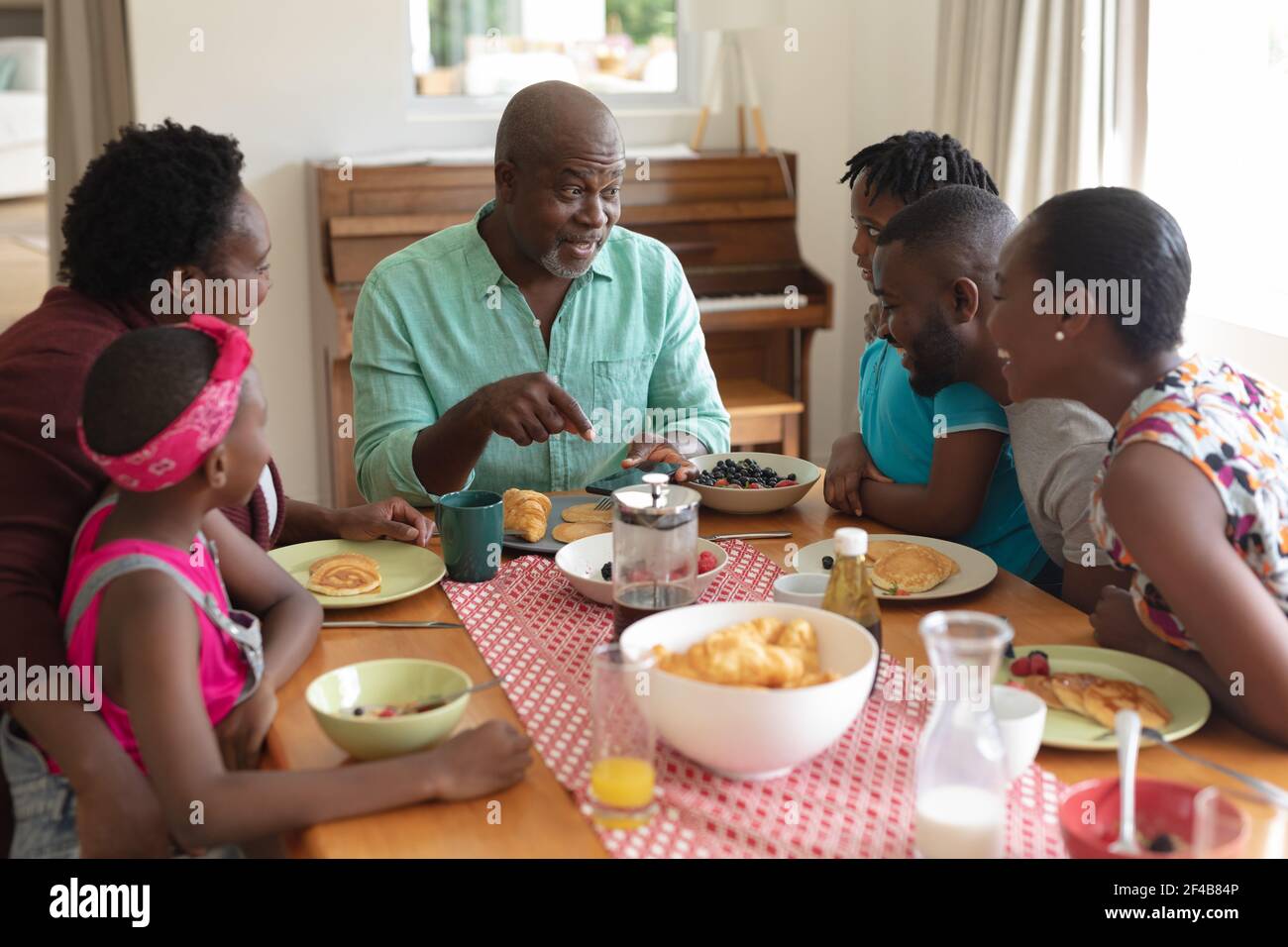 Glücklicher afroamerikanischer Großvater im Gespräch mit Enkelkindern und ihren Eltern Beim Familienessen Stockfoto