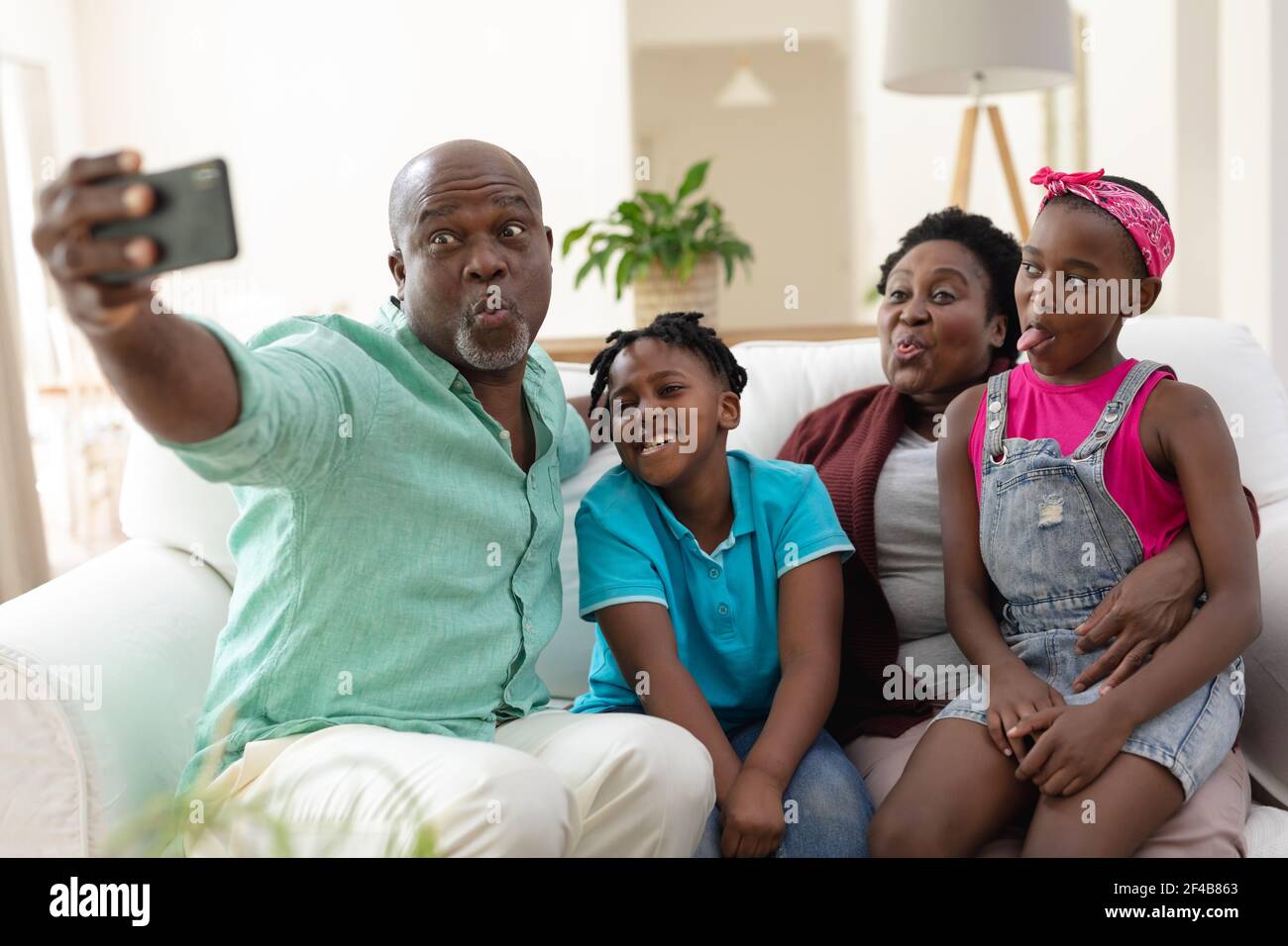 afroamerikanische Großvater und Großmutter auf Couch machen Gesichter mit Enkelkinder nehmen Selfie Stockfoto
