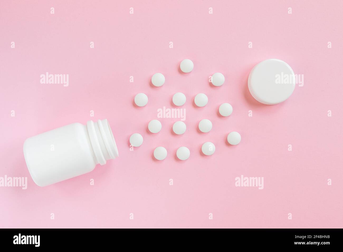 Weißes Glas und verstreute weiße Pillen auf einem rosa Hintergrund. Medizin und Gesundheitswesen Konzept. Draufsicht Stockfoto
