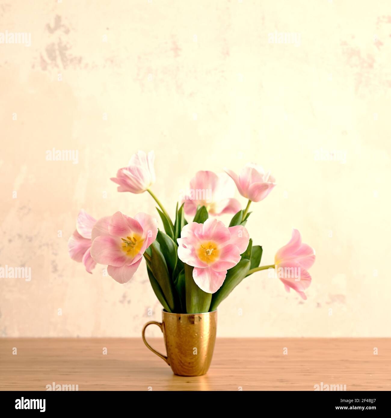 Sommer-Vibes und Stimmung Bild von Bouquet von rosa Tulpen In goldenem Becher auf dem Tisch Stockfoto