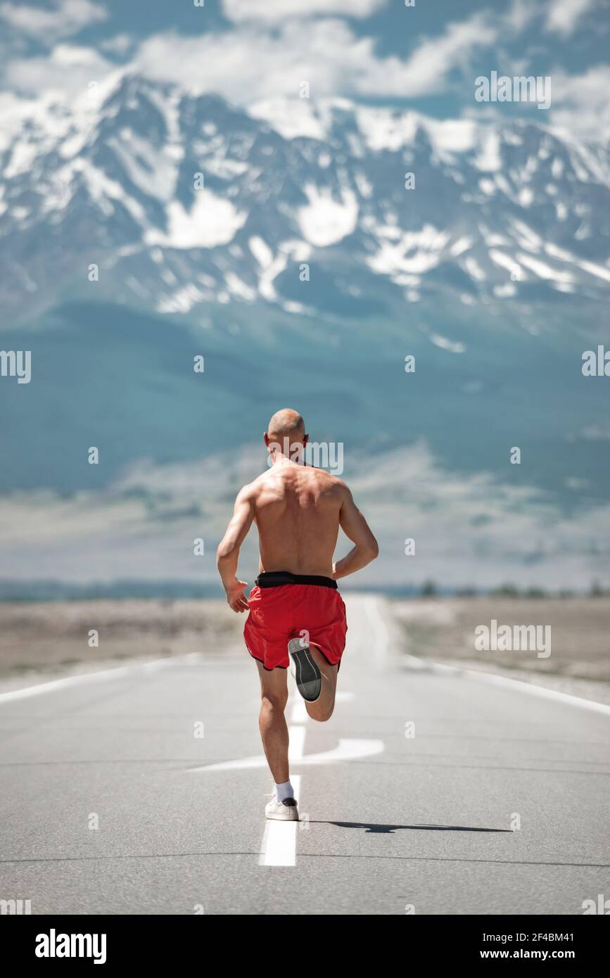 Der sportliche Mann Jogger läuft an einer geraden Bergstraße entlang. Fitnesskonzept im Freien Stockfoto