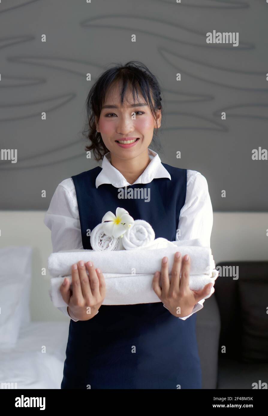 Junge Hoteldame mit einem Lächeln und einem Handtuch mit weißer Blume. Das Personal in blauer Uniform bereitet die Zimmer für die Hotelgäste vor. Stockfoto