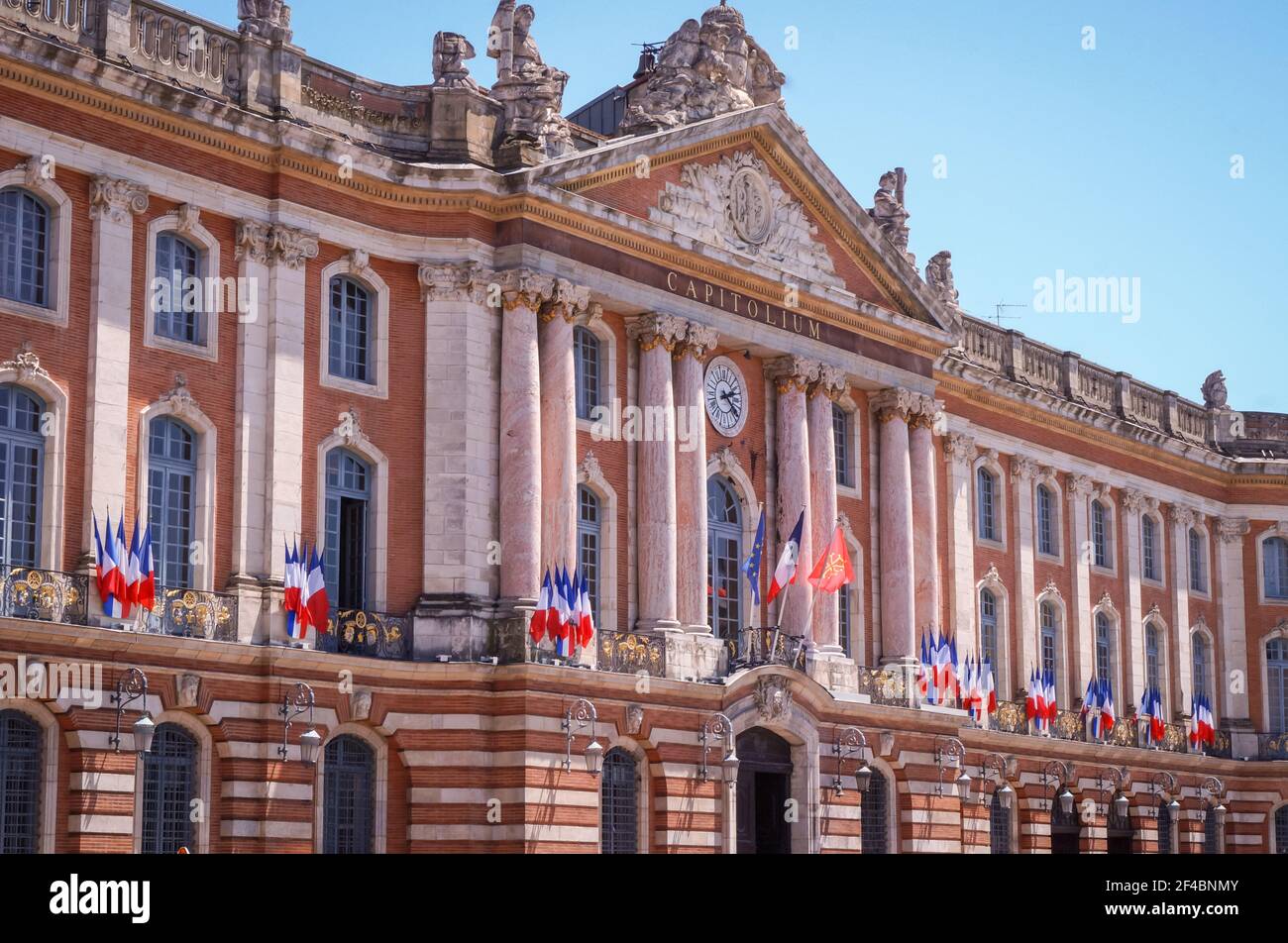 Die monumentale Backsteinfassade des Capitole, das klassische Gebäude des Rathauses, in Toulouse, Frankreich, geschmückt mit französischen Flaggen zum Tag der Bastille Stockfoto