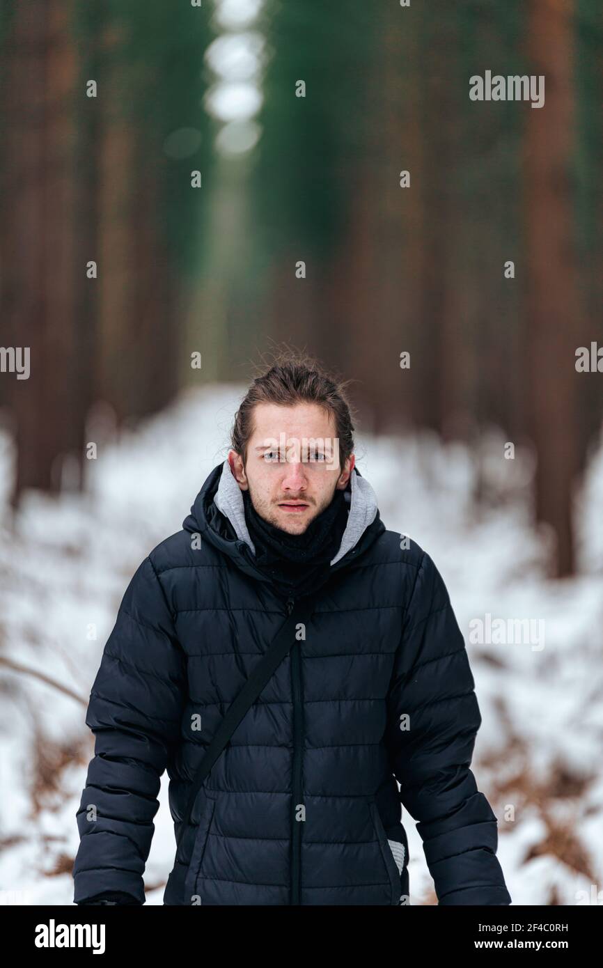 Hübscher junger Mann, der in einem verschneiten Wald steht und gerade aussieht In die Kamera Stockfoto