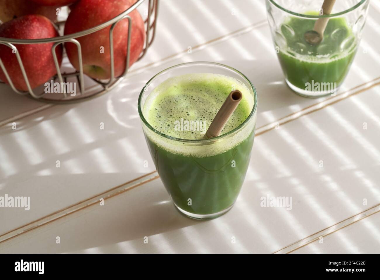 Ein Glas grünen Saft mit einem Bambusstroh, mit Äpfeln im Hintergrund Stockfoto