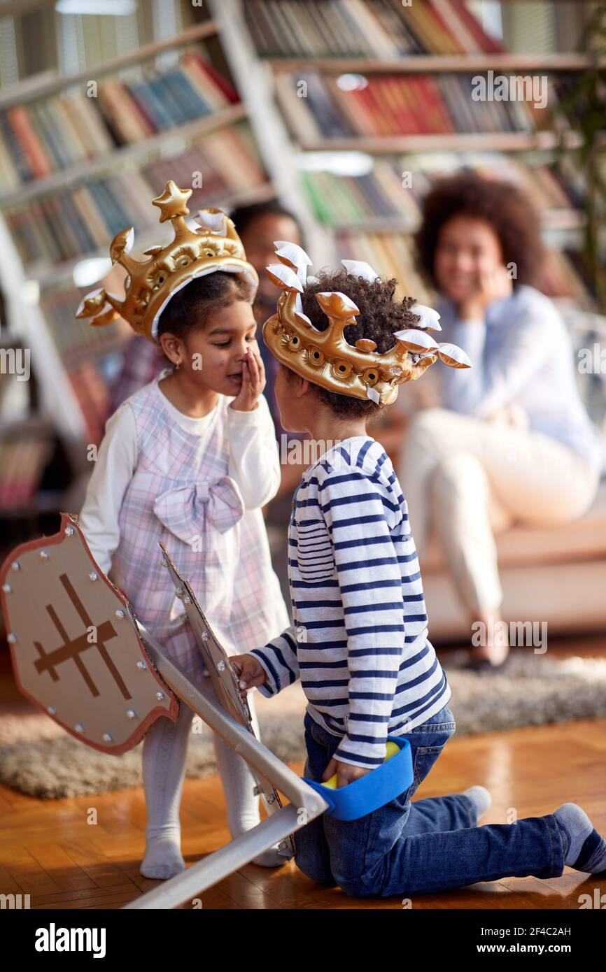 Kinder, die als Ritter gekleidet sind, flüstern und murmeln, während sie eine Zeit mit ihren Eltern in einer entspannten Atmosphäre zu Hause verbringen. Familie, Haus, playtim Stockfoto