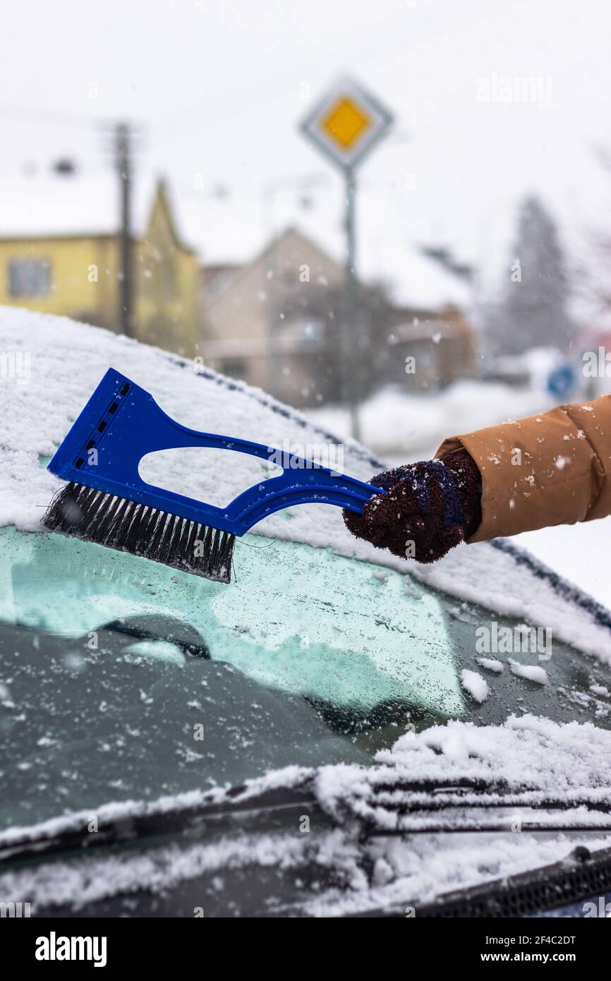 Reinigung der Windschutzscheibe von Schnee durch Eiskratzer mit Bürste im Winter. Schnee vom Auto auf der Straße entfernen. Stockfoto