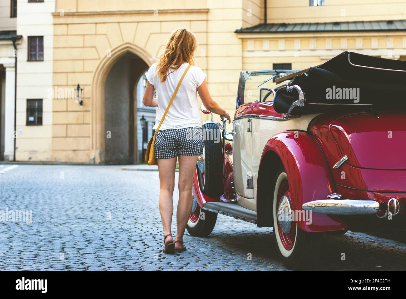 Junge Frau und Retro-Oldtimer in der Altstadt. Frau öffnet die Tür eines Retro-Autos und verlassen Stadt für einen Urlaub. Stockfoto