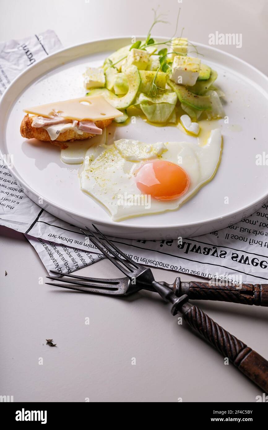Leckeres und gesundes Frühstück. Spiegelei und Gemüsesalat mit Avocado und Kräutern. Mini-Croissant mit Schinken und Käse auf einem runden weißen Teller. Orga Stockfoto