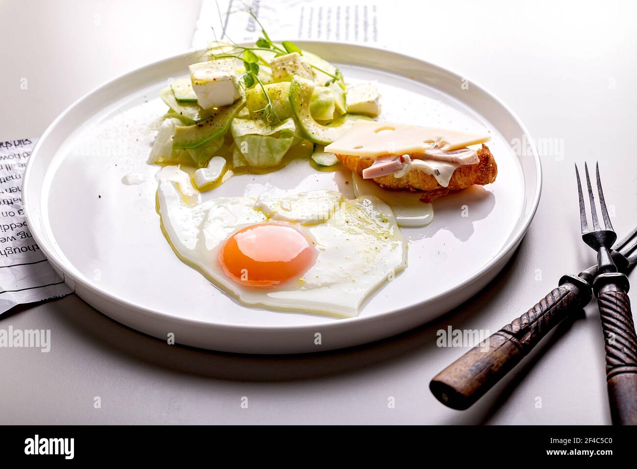 Leckeres und gesundes Frühstück. Spiegelei und Gemüsesalat mit Avocado und Kräutern. Mini-Croissant mit Schinken und Käse auf einem runden weißen Teller. Orga Stockfoto
