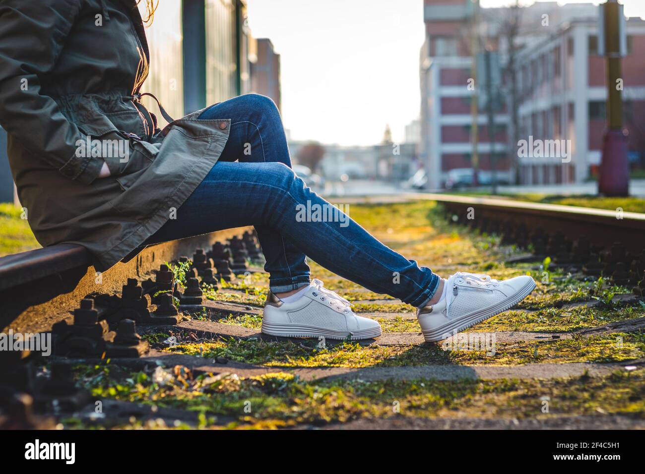 Frau in legerer Kleidung und weißen Sneakers auf Schienen sitzend. Entspannung in der Stadt. Modekonzept Stockfoto