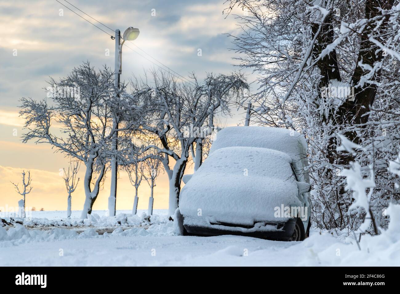Schneebedecktes Auto, das neben der Straße mit Straßenlaternen geparkt ist. Winterschneehaltung. Stockfoto