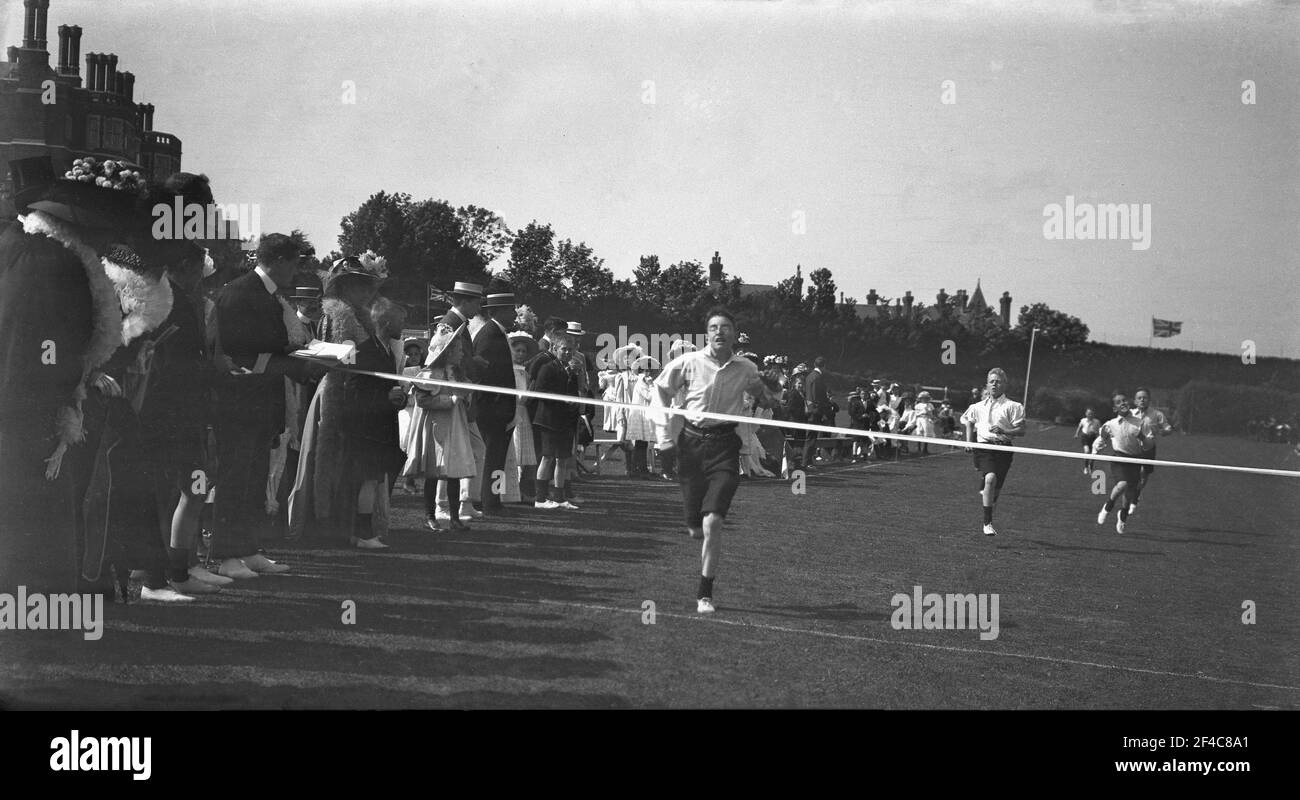 1930s, historisch, draußen auf einem Spielfeld, beobachtet von Zuschauern, einige in Strohboothüten, öffentliche Schüler, die an einem Laufrennen teilnehmen, mit einem Jungen, der kurz davor steht, das Zielband zu überqueren, England, Großbritannien. Stockfoto