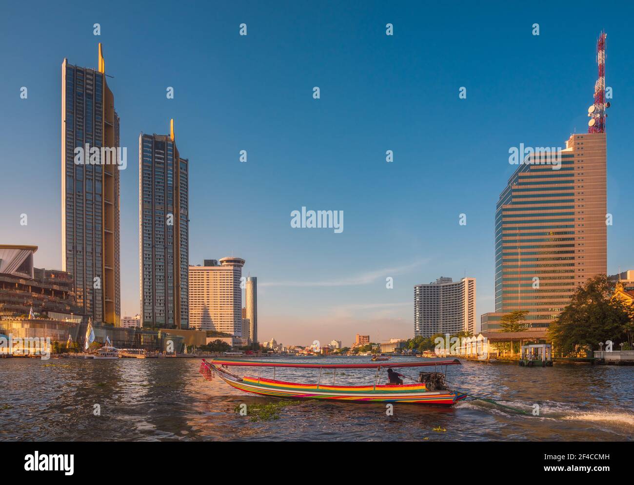 Wolkenkratzer und traditionelles Long Tail Speedboot auf dem Chao Phraya Fluss in Bangkok, Thailand während der Goldenen Stunde Stockfoto