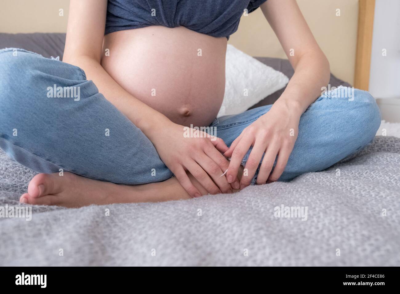 Vorderansicht der jungen erwachsenen schwangeren Frau, die im Bett in Lotusposition sitzt und Meditation praktiziert, Konzept HLS, Yoga Stockfoto