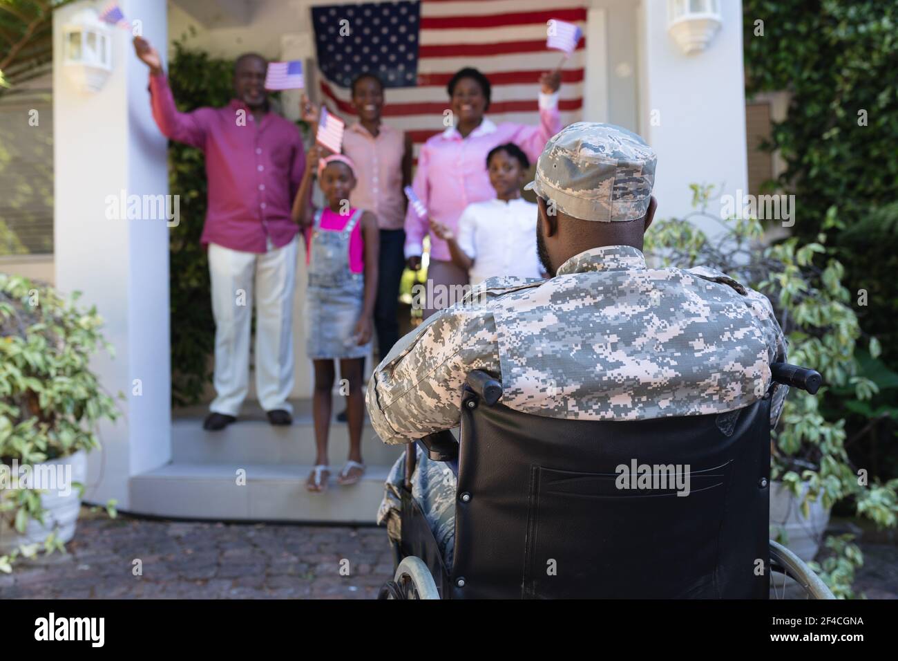 afroamerikanischer Soldat Vater im Rollstuhl Begrüßung lächelnd drei Generation Familie außerhalb des Hauses Stockfoto
