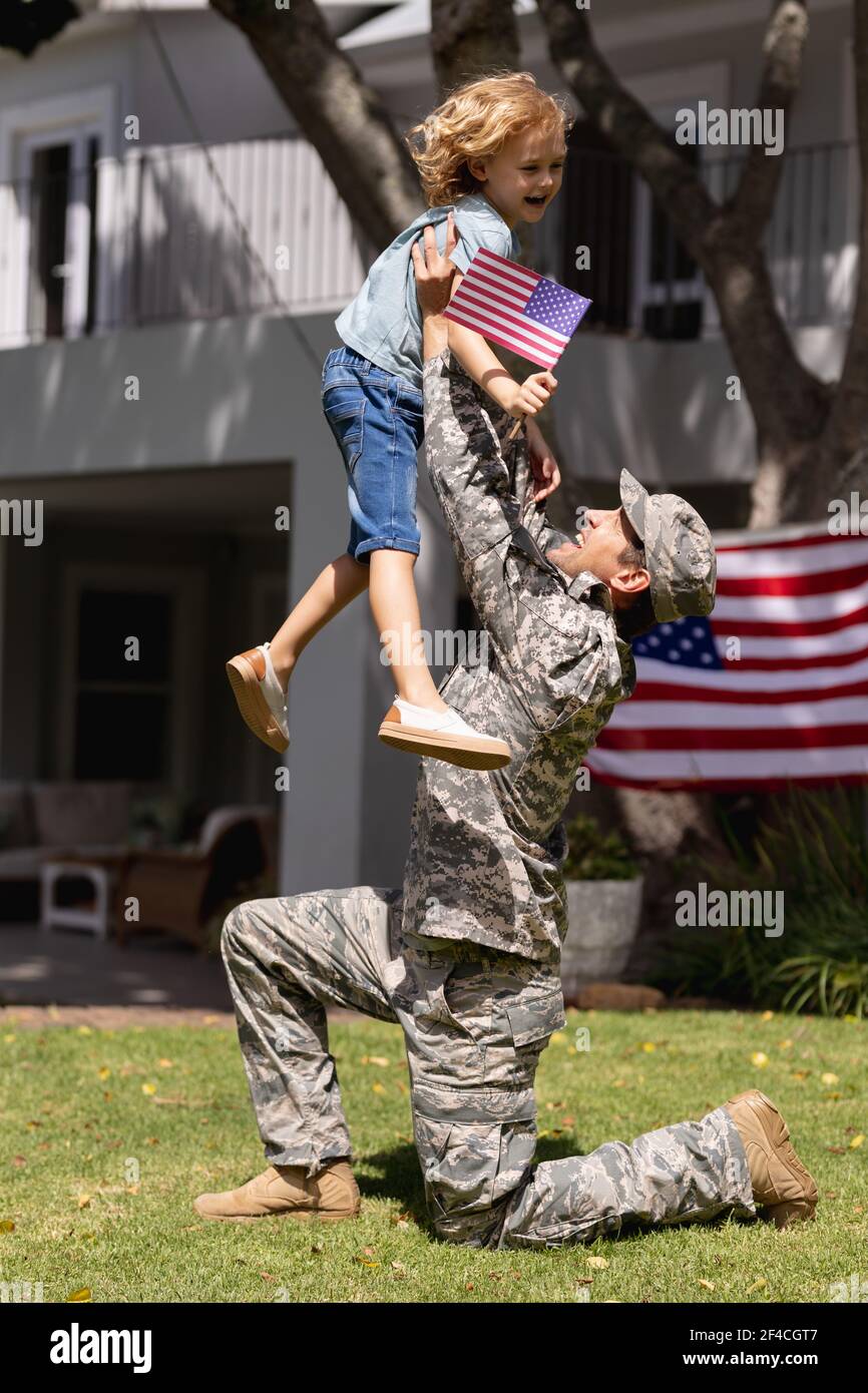 Lächelnd kaukasischen Soldaten Vater glücklich Sohn im Garten mit amerikanische Flagge vor dem Haus Stockfoto