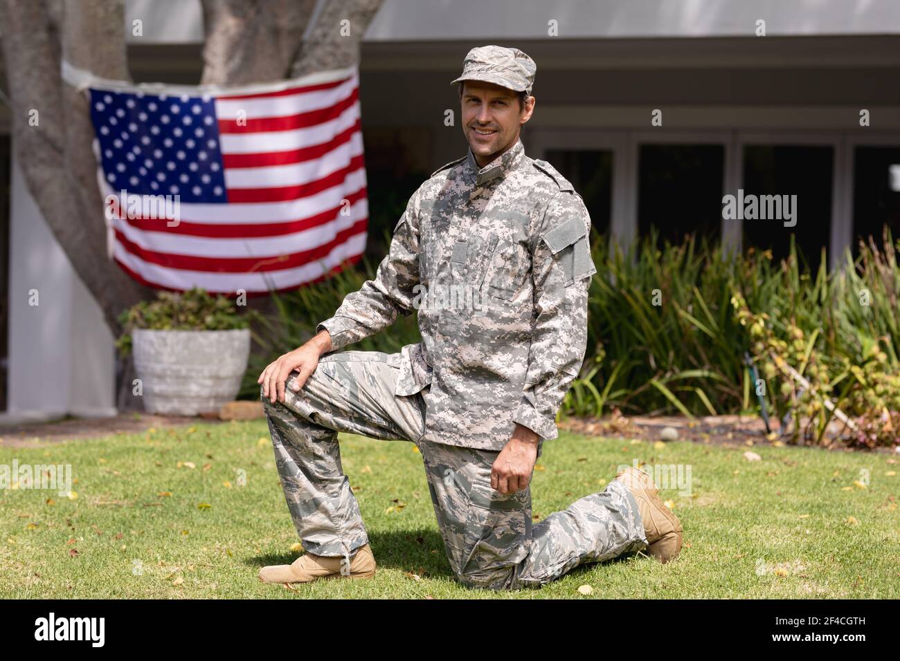 Lächelnder kaukasischer Soldat Vater kniet im Garten mit amerikanischer Flagge Hängen vor dem Haus Stockfoto