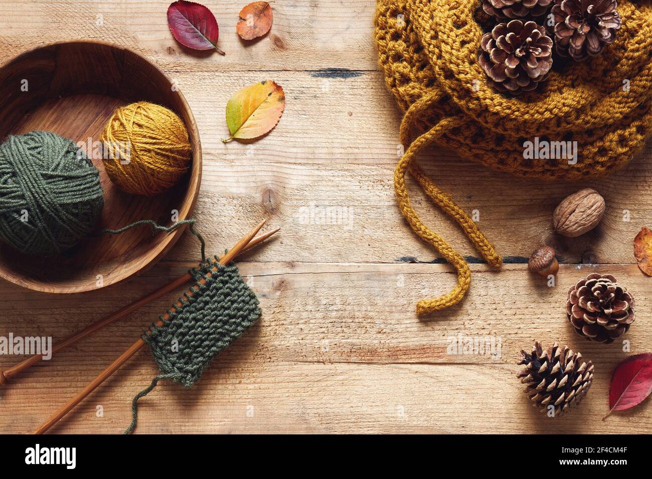 Ein Stück Stricken mit Holznadeln und Garn zwischen Blättern und Tannenzapfen, Herbst Stricken. Stockfoto