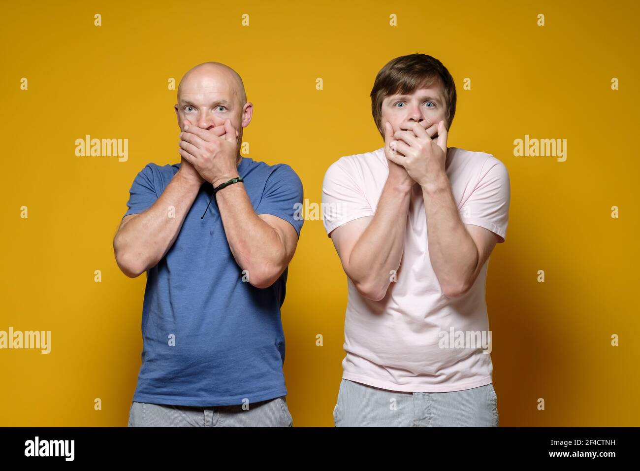 Zwei verängstigte Männer bedeckten ihren Mund mit ihren Händen, sie haben Angst, ein Geheimnis zu erzählen und blicken ängstlich auf die Kamera. Stockfoto