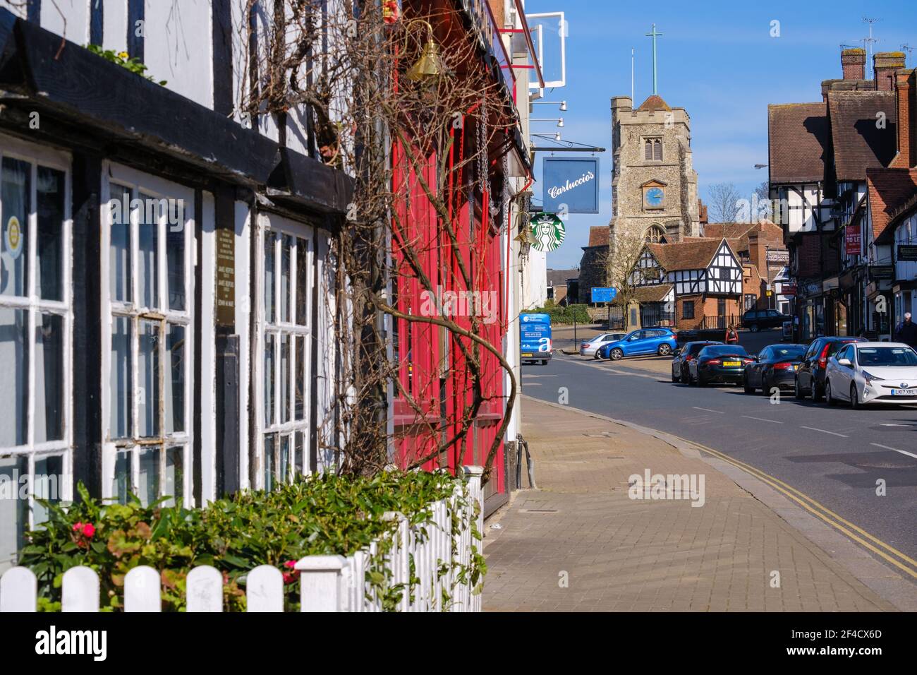 Pinner Village High Street mit Carluccios Restaurant & Starbucks auf der linken Seite & Saint John the Baptist, mittelalterliche Kirche auf einem Hügel im Hintergrund. Stockfoto