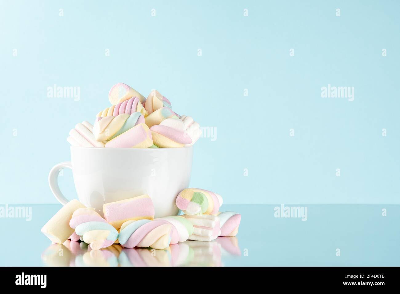 Marshmallows bunte Kaubonbons in einer Tasse auf blauem Hintergrund. Sweet Holiday Food Konzept. Stockfoto