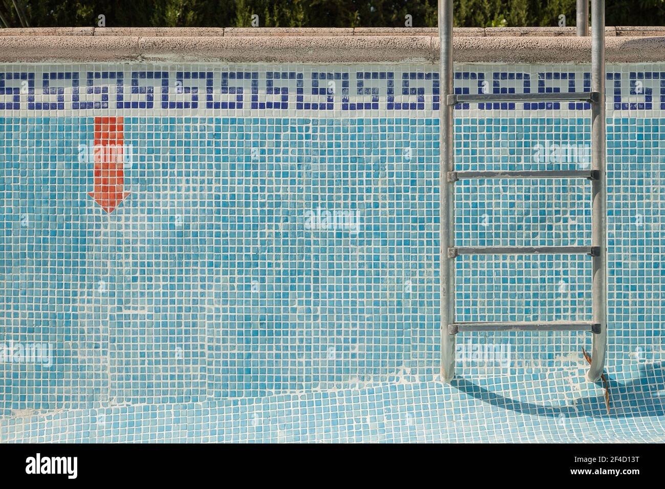 Gefliester Pool ohne Wasser mit einer Leiter und einem roten Pfeil nach unten Warnschild. Strukturierter Hintergrund. Stockfoto