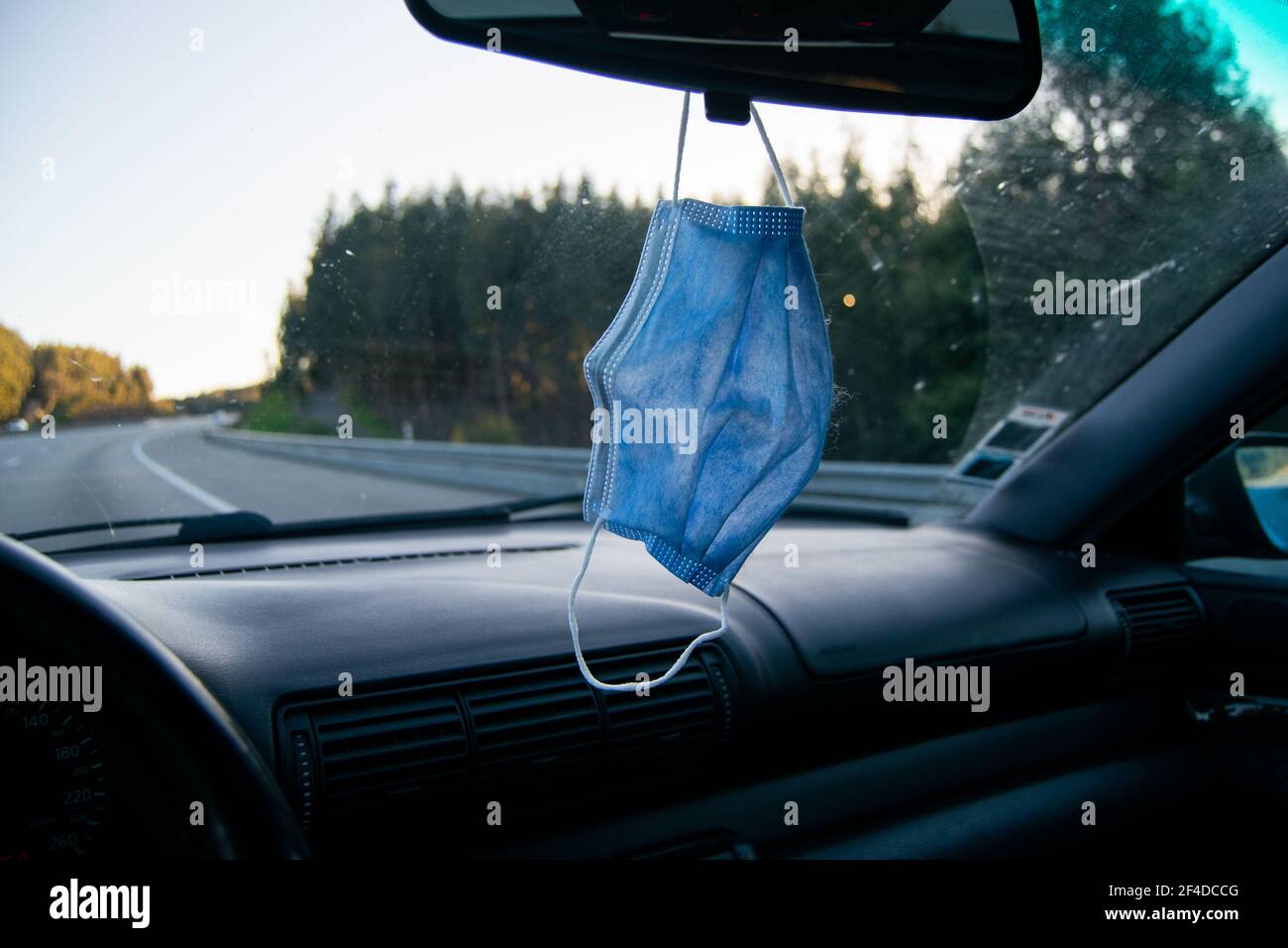 Fahren eines Autos mit Covid19 Maske hängen auf dem Auto Rückansicht Glas. Fahren oder Autofahren in covid19-mal mit der benötigten Maske auf dem Auto. Stockfoto