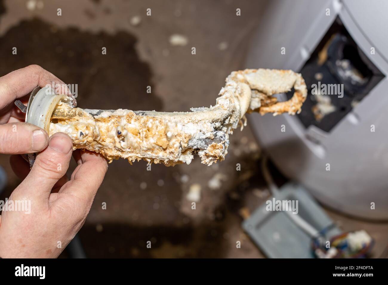 Reparatur und Wartung von Kesseln. Der Meister Klempner nahm es aus dem Kessel und hält in seinen Händen eine röhrenförmige elektrische Heizung mit Kalkablagerungen bedeckt. Stockfoto