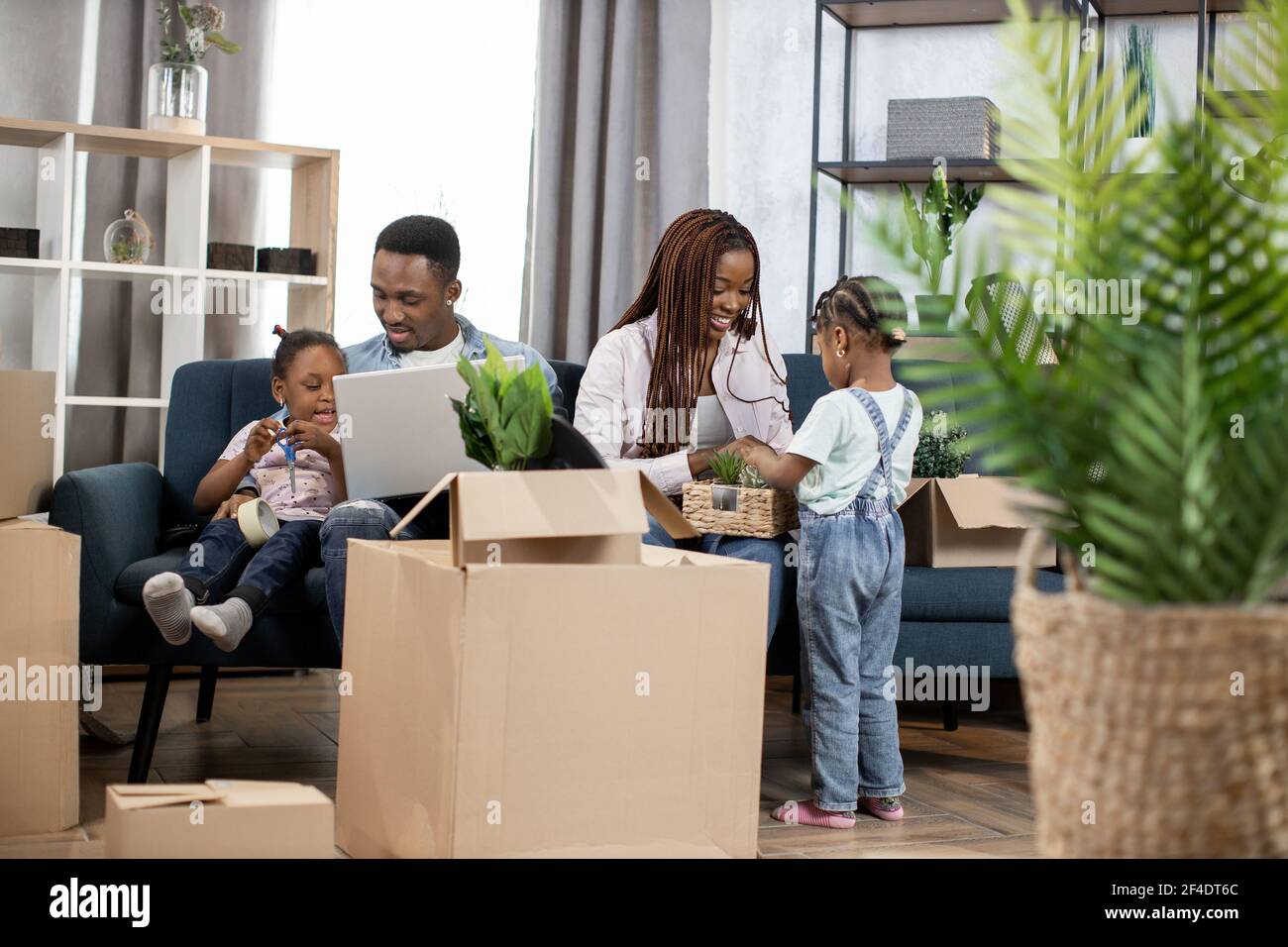 Hübsche afro amerikanische Töchter helfen Eltern zu packen Boxen für Umzug. Junge Familie bereitet sich auf den Umzugstag vor. Besitzer der neuen modernen Wohnung. Stockfoto