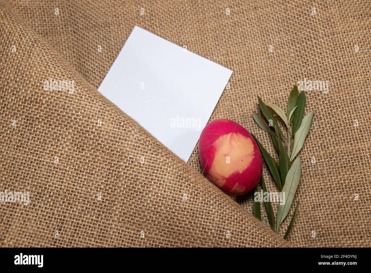 Gefärbtes Ei und ein Olivenzweig auf einem Jutetuch mit einer blanck-Karte für Ostern gedacht. Stockfoto