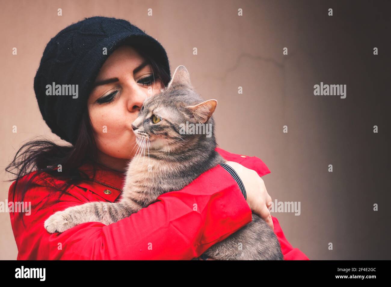 Eine Frau in Rot hält und küsst eine Katze mit Tabby Stockfoto