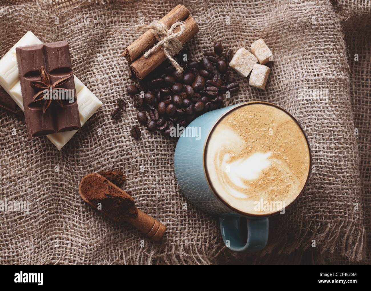 Große Tasse Kaffee mit Zimt, Anis, Kaffeebohnen, Schokolade auf Holzhintergrund oben Stockfoto